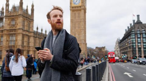 Man using smartphone in front of the Houses of Parliament in Westminster