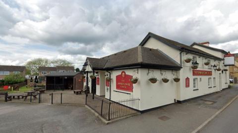 Exterior of The Cambridgeshire Hunter pub - a view from the street, also showing a section of the beer garden and car park 