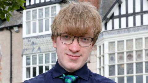 A man with short brown hair and glasses wearing a blue shirt