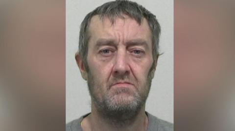 Mugshot of Robinson. He has a scruffy grey beard and messy greying hair.