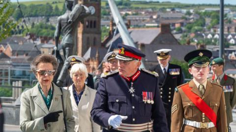 A groups of people, some in naval uniform, walk across Derry's Ebrington Square. Two of the people are women, in the company of five uniformed men