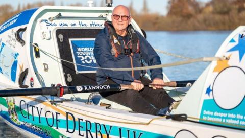 Vic Handley on his boat wearing glasses and holding a pair of oars