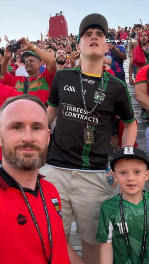 Two men and a teenager stand with the world cup tickets. The man in the red football shirt has a little boy on his shoulders.