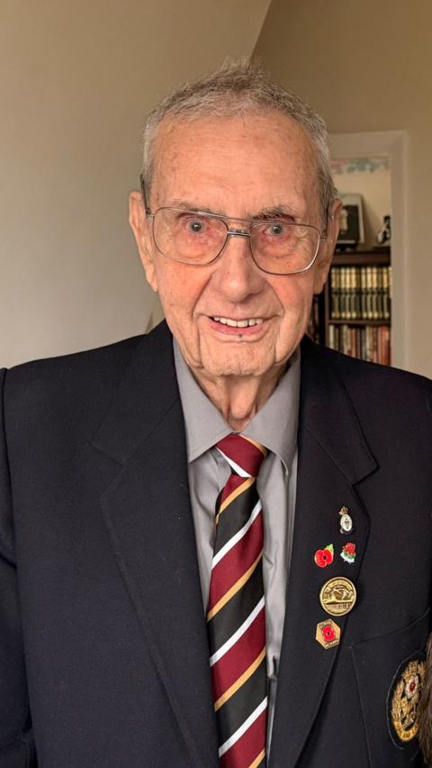 Arnold, a WW2 veteran who is wearing a suit with several poppies and an army medal