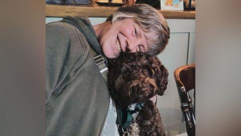 Louise Parkin wearing a grey hoodie smiling with her dog Murphy.