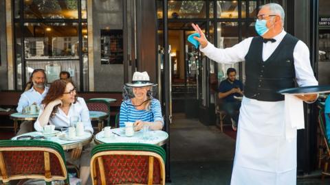 A waiter gestures towards customers in Paris