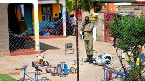 An Ugandan police officer secures the scene at a school after a man posing as a parent stabbed and killed children there, in Kampala, Uganda