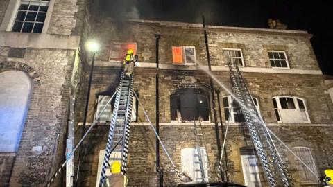 Ryde former theatre and town hall with smoke coming from the building and flames from the windows - firefighters are on ladders and at street level fighting the fire.