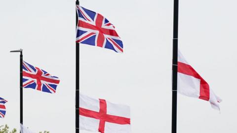 A set of union jack and St George's flags attached on lampposts on a cloudy day.