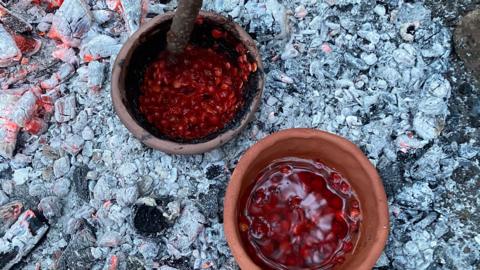 Berries crushed in a clay pot sat on grey coals from the fire