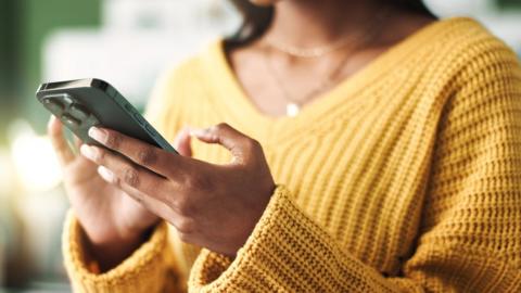 Close-up of a woman wearing a yellow jumper holding a smartphone