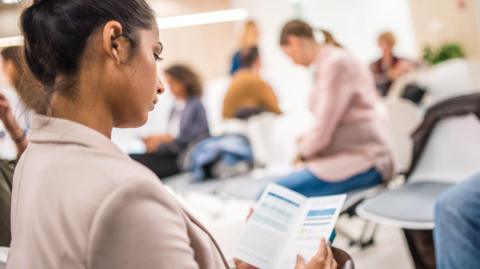 Young woman reading brochure in clinic waiting room.