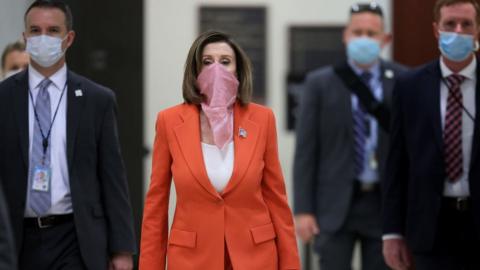 Wearing a scarf over her mouth and nose, Speaker of the House Nancy Pelosi (D-CA) is surrounded by security and staff as she arrives for her weekly news conference during the novel coronavirus pandemic at the US Capitol 24 April, 2020 in Washington, DC