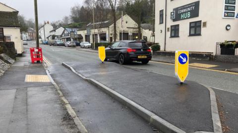 A view of a built-out section near a building signed Community Hub with obvious damage to the corner kerb stone