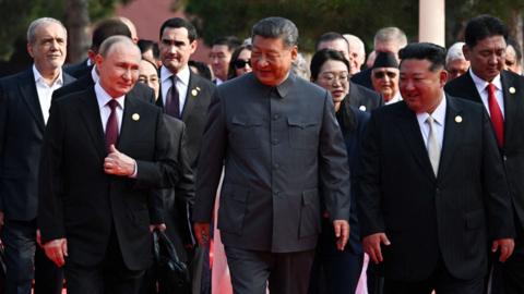 Vladimir Putin, Xi Jinping and Kim Jong Un walking side by side with other world leaders behind them