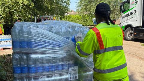 A man in a high-vis yellow jacket collecting bottles of water.