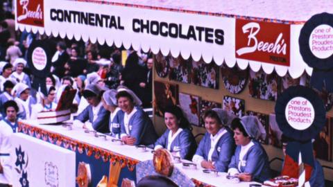 Members of Beech's Fine Chocolates workforce wearing blue and white aprons and hair nets running a stall at Preston Guild.