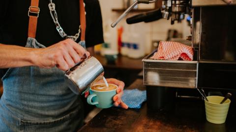 A stock photo of someone pouring milk into a coffee cup