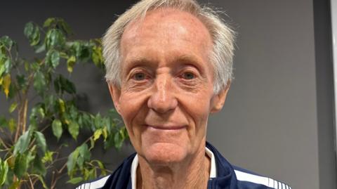 A close-up of Geoff. He has short grey hair and is smiling. He is wearing a sports jacket.