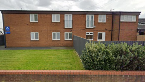 Westmead carehome in Castleford sits behind a wall and lawn. A fence runs through the grass which features a hedge in front of it.