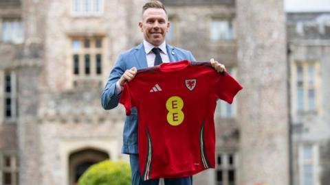 New Wales boss Craig Bellamy holds up the team's shirt