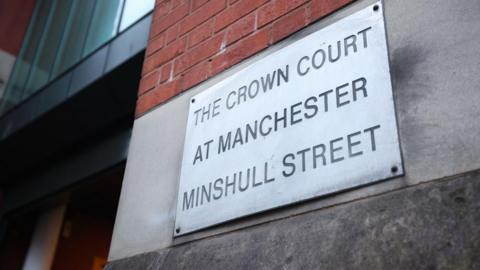 A sign nailed to a brick wall reads 'The Crown Court at Manchester Minshull Street'. 