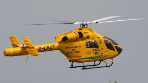 A yellow helicopter in mid flight, the sky is grey