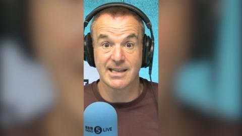 Martin Lewis in a BBC studio wearing headphones, with a blue microphone in front of him
