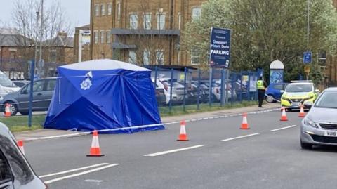 A blue police tent on a main road with police, a police car and cones