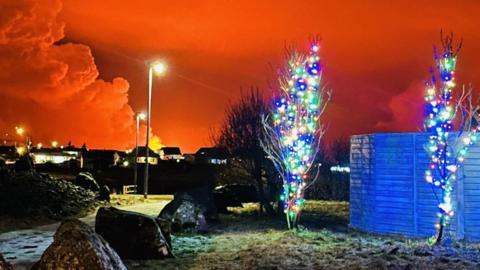 Smoke billows into the air in Iceland as a volcano erupts - Christmas lights can also be seen