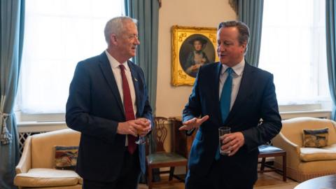 Benny Gantz and Lord Cameron pictured chatting in a room with blue curtains and a gold-framed portrait behind them