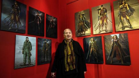 Lindy Hemming poses in front of her costume designs is on display at the DC Comics Exhibition: Dawn Of Super Heroes at the O2 Arena