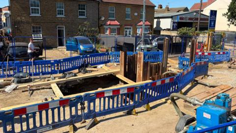 Roadworks shows hole in ground and red/white/blue fences around it