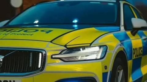A close up of the front and side of a police car with yellow and blue checked markings  