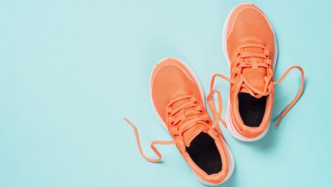A pair of orange running shoes on a light blue background