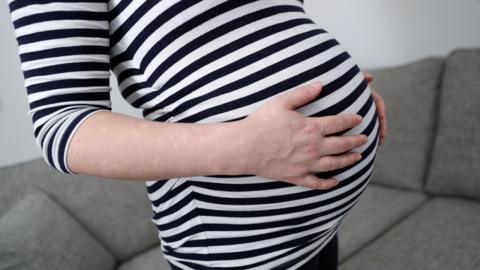 A pregnant woman wearing a black and white striped shirt holding her belly 