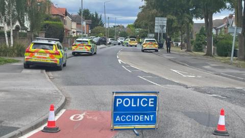 Residential road with four police cars parked along it and a police warning sign in foreground