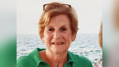 The picture shows Judith Brown wearing a green shirt, in the background is the sea. 