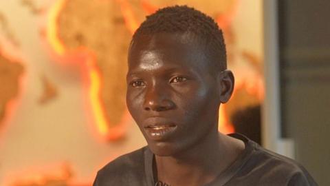A head-and-shoulders image of Rasheed Wasiu wearing a black T-shirt. Out of focus, in the background, a map of the globe can be seen.