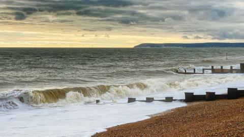 The waves of a grey sea crash on a pebble beach. 