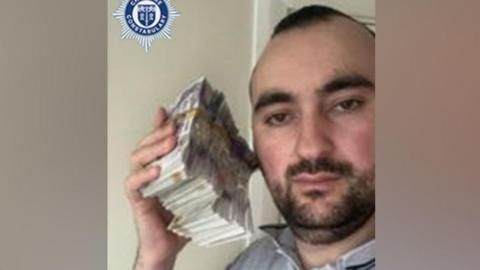 A man is holding a bundle of cash next to his head