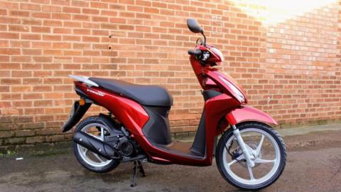 A red moped in front of a brick wall