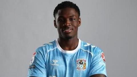 Jahnoah Markelo poses with arms crossed in a sky blue Coventry City shirt after signing for the club