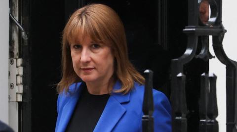 Chancellor Rachel Reeves wearing a dark blue jacket emerges from the doorway of 11 Downing Street 