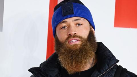 Ashley Cain with a beard wearing a blue beanie hat, looking to the camera.
