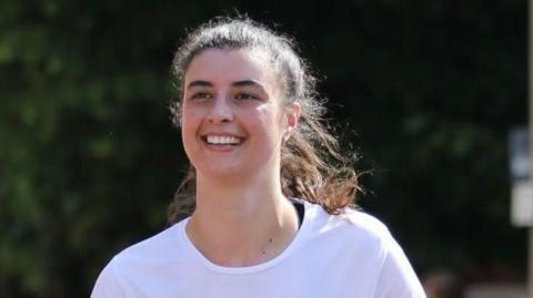 Harriet Davidson running a 10k race. She has long brown hair tied back in a ponytail and is wearing a white t-shirt.