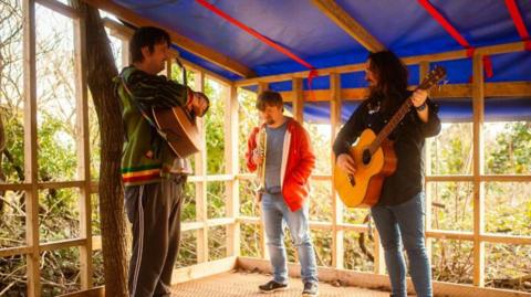 Three people standing with different instruments like guitars