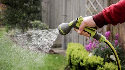 A hand holding a garden hose with water dripping from it