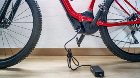A close up of a red electric bike with a charger plug attached