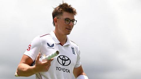 Asa Tribe of the England Lions walking off the field with a bat tucked in between his right arm.